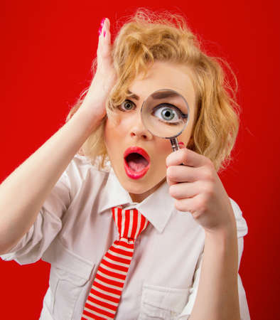 Amazedly funny woman with magnifier, isolated on red backgroundの写真素材