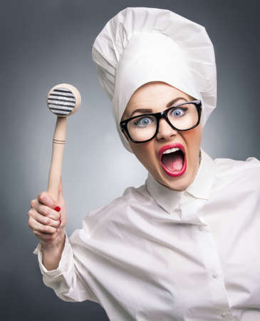 Mad woman cook with a hammer punching you, isolated on gray. Humorous conceptの写真素材