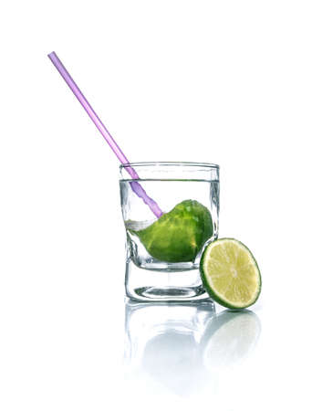 Cold drink with lime and drinking straw. Glass beaker with vodka over white background