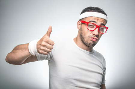 Funny sport man gesturing thumbs up, isolated on gray background. Nerd doing fitnessの写真素材