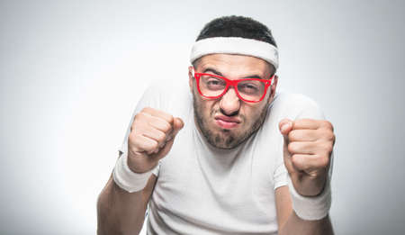 Funny nerd doing aerobics showing his fists, isolated on gray background, studio shot. Crazy sport...