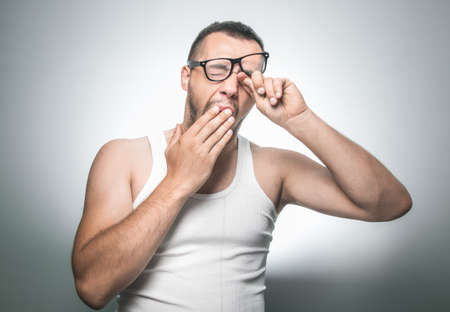 Guy waking and yawning, isolated on gray background, studio shot. Funny drowsy man with hand -...