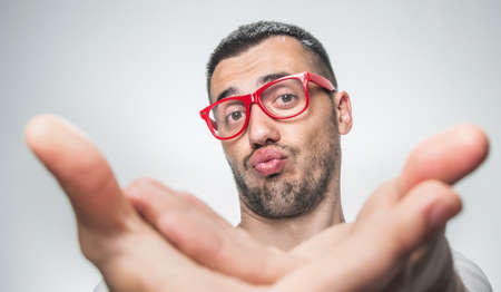 Funny selfie. Young man holding camera and making selfie with facial expression. Purched lips. Nerd close up isolated on gray backgroundの写真素材