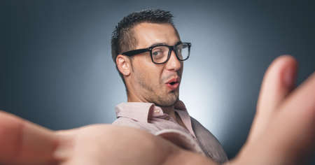 Selfie. Funny young man taking a selfie photo over dark gray background. Studio shotの写真素材