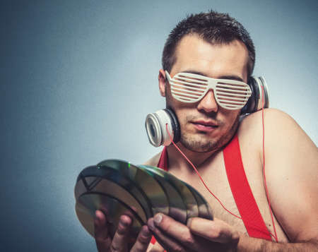 Dj holding CDs, guy is ready for party. Young trendy man listening music with headphones over dark...