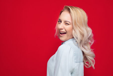 Amusing woman winking and posing, isolated on red background. Playful cute girl. Studio shotの写真素材