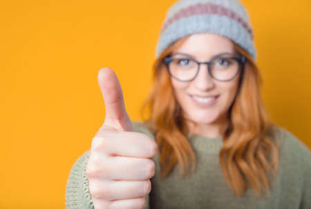 Young smiling girl with thumb up, like concept. Focus on finger. isolated on yellow background. Yes...