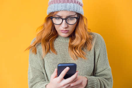 Mistake. Panicked young woman with the mobile phone in the trouble, no time concept, isolated on yellow background. Worried girl looking to phone. Studio shotの写真素材