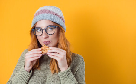 Closeup young woman eating cookies. Beautiful girl enjoying in sweet food, delicious snack, isolated on yellow background. Studio shotの写真素材