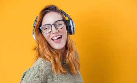 Cheerful young woman with earphones enjoying while listen music, isolated on yellow background. Profile of joyful woman with earphones. Happiness concept. Studio shotの写真素材