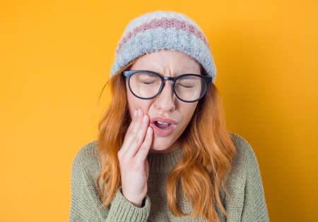 Toothache. Young woman suffering from teeth pain, isolated on yellow background. Studio shotの写真素材