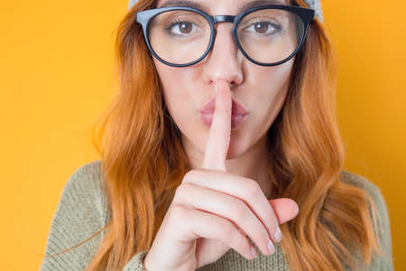 Hush. Young woman holding finger on lips, keep the secret concept, isolated on yellow background. Studio shotの写真素材