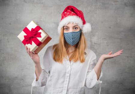 Beautiful blond woman wears christmas santa claus hat - cap and holding red gift box - present with ribbon, isolated on gray background.の写真素材