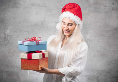 Santa woman holding christmas gifts isolated on gray background. Happy young girl wearing red santa...