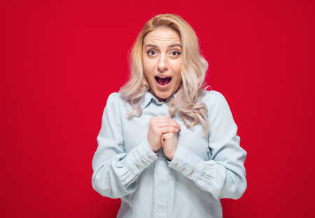 Unbelievable. Thrilled woman with opened mouth and clenched fists, isolated on red background. Female person with surprised expression. Yes concept. Good news. Studio shotの写真素材