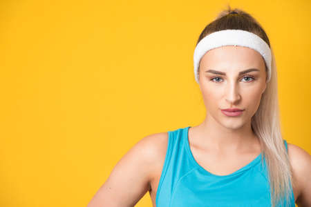Serious young sportswoman looking at camera and wearing sport clothing - sportswear, isolated on yellow background. Front view portrait of a cute fitness girl. 80s styling. Studio shotの写真素材