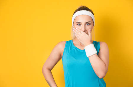 Astonished vitality woman covers her mouth, isolated on yellow background. Surprised fitness girl. Unbelievable concept. 80s styling. Studio shotの写真素材