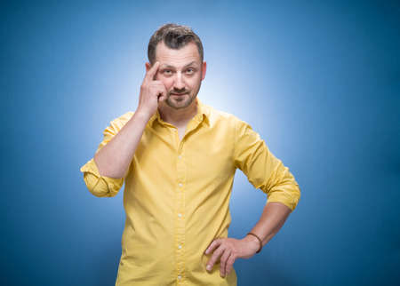 Crafty young man asking. Copy space over blue background, dresses in yellow shirt. Half length guy at the ask concept. Studio shotの写真素材