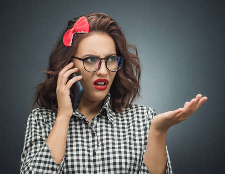 Upset woman on the phone over dark gray - black background. Annoyed girl talking. Studio shotの写真素材