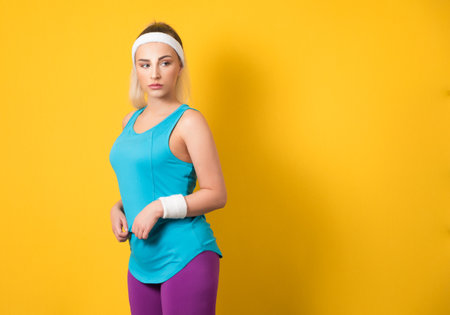 Fitness young woman posing and looking to side, isolated on yellow background. Half length of sportswoman ready for exercising. Athletic female person. 80s styling. Studio shotの写真素材