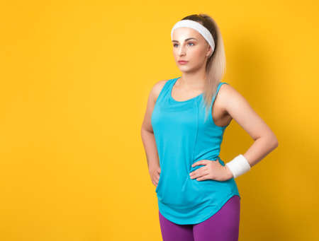 Fitness young woman posing and looking to side, isolated on yellow background. Half length of sportswoman ready for exercising. Athletic female person. 80s styling. Studio shotの写真素材