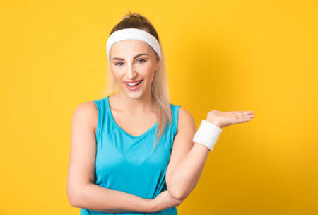 Fitness woman holding free advertising space for your product on her palm, copy space. Isolated on white. Half length of sportswoman doing presentation. Athletic female person. 80s styling. Studio shotの写真素材