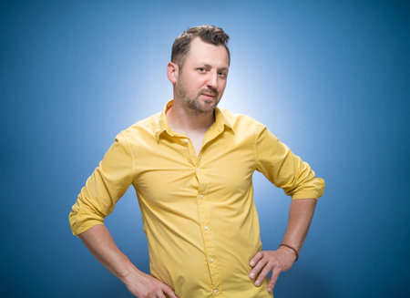 Amused thoughts young man thinking. Portrait of inspired guy over blue background, dresses in yellow shirt. Studio shotの写真素材