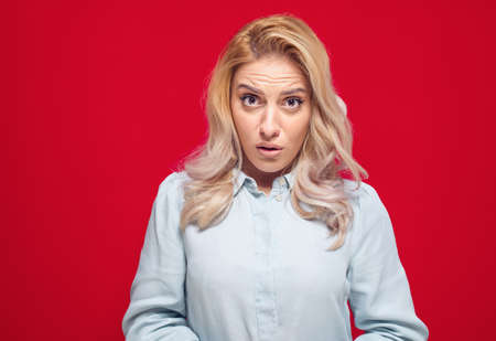 Impressed young woman looking at camera and say what, isolated on red background. Studio shotの写真素材