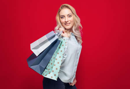 Cheerful shopping woman holding package bag with purchases after shopping, isolated on red background. Studio shotの写真素材