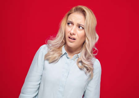Suspect concept. Distrustful young woman, isolated on red background. Studio shotの写真素材