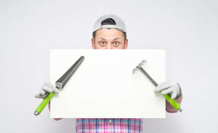 Male gardener behind white board holding gardening tools, isolated on white background. male farmer showing blank empty paper billboard with blank space near her head. Studio shotの写真素材