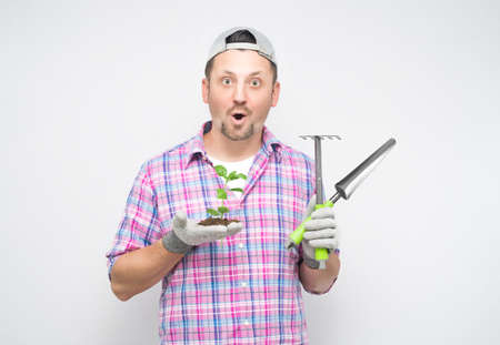 Surprised male gardener with plant and gardening tools, isolated on white background. Amazed male farmer. Studio shotの写真素材
