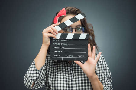 Young woman holding movie clapper board over dark gray - black background. Studio shotの写真素材