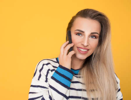 Happy young woman talks on the phone, isolated on yellow background. Female person using the smartphone. Studio shotの写真素材