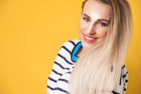 Face of nice girl keeps chin on shoulder, isolated on yellow background. Closeup portrait of a cheerful woman. Studio shotの写真素材