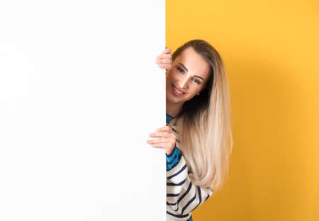 Smiling young women holding white board, isolated on yellow background. A beautiful girl showing blank empty paper billboard with blank space for text. Studio shotの写真素材