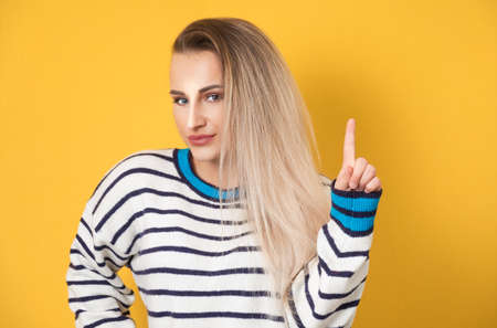 Young woman pointing up with forefinger to copy space - blank space for text, isolated on yellow background. Studio shotの写真素材