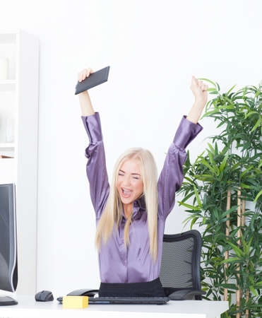 Successful young blonde businesswoman, victory gesture, hands up, smiling at officeの写真素材