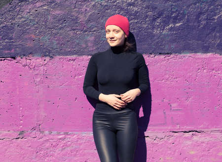 woman in black standing at the colorful wall in a red cap