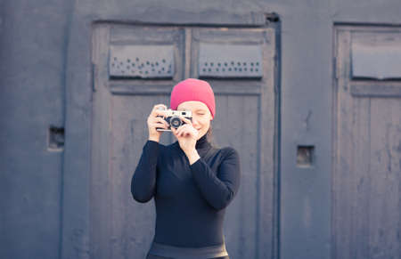 the girl in black clothes at a black textural wall photographs the vintage camera.