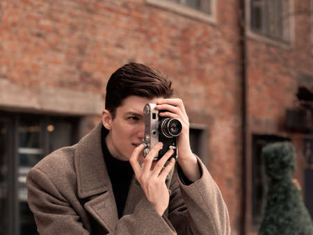 the young man in a coat photographs model the vintage camera at a metal rusty wall