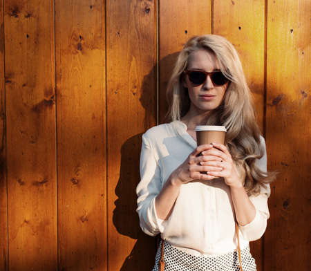 Young sexy blonde girl with long hair in sunglasses holding a cup of coffee have fun and good mood...