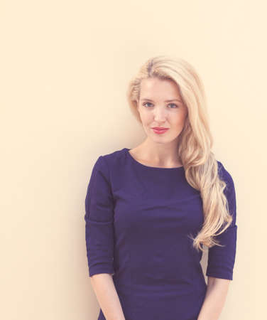 Summer portrait of young beautiful blond woman in blue dress posing near the wall