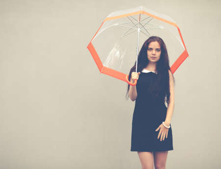 Beautiful brunette with long hair in a short black dress standing under a transparent umbrellaの写真素材
