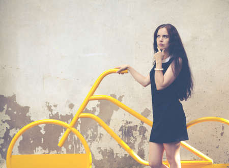 Beautiful brunette with long hair standing in thought near a yellow bikeの写真素材