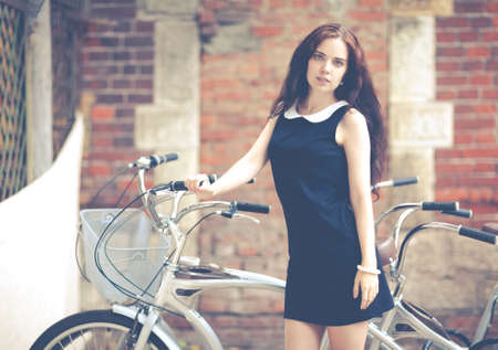 Beautiful brunette with long hair standing near a bikeの写真素材