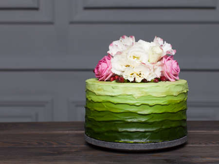 Beautiful green cake decorated with flowers stands on dark wooden board