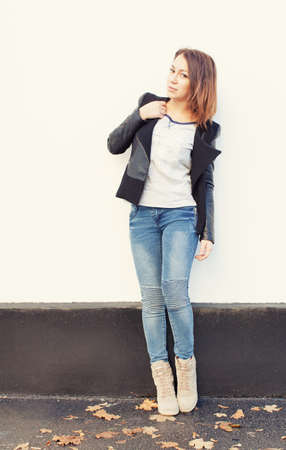 Beautiful brunette girl posing near the wall in blue jeans and a black jacketの写真素材
