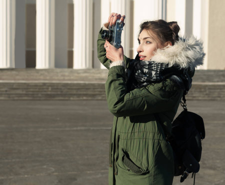The girl in the green jacket photographs vintage camera outdoors on a sunny spring dayの写真素材