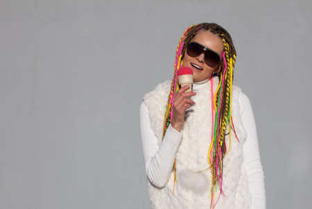 Beautiful girl with colored dreadlocks summer sunny day in a white jacket with sunglasses eating pink ice cream on the streetの写真素材